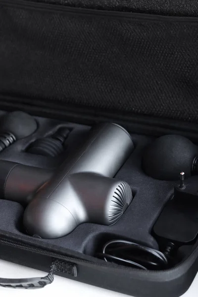 Machine for body massage. Massage percussion device with different of nozzles. Electric massager gun for body massage in a case on a black background.