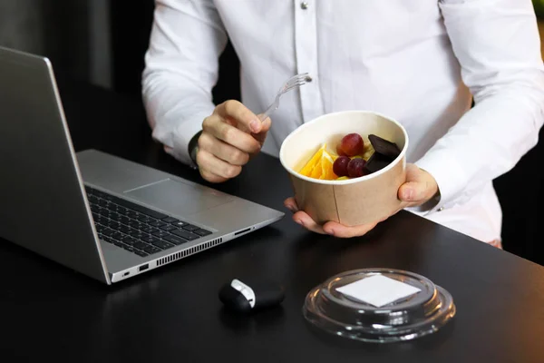 Healthy lunch at office workplace. Man eating nutrition lunch from takeaway container at working table with laptop.