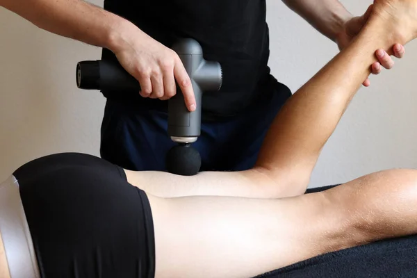Spor salonunun tıbbi odasında spor perküsyon masajı. Masör masaj egzersizleri yapıyor. Spor vücut masajı için perküsyon terapisi. Spor sakatlıklarının rehabilitasyonu