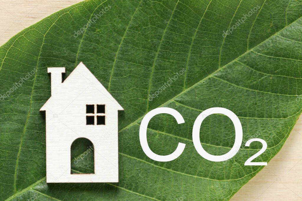 Decarbonization of Real Estate. Lower CO2 emissions and reduce carbon. Wooden House, letter CO2 on green leaf background. Sustainable development, environment protection