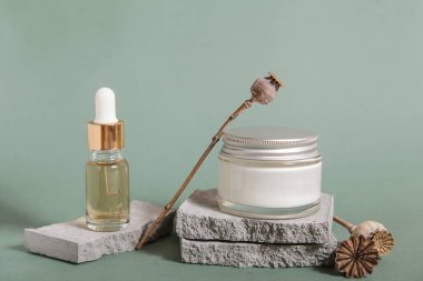 Kurutulmuş haşhaş tohumu, kozmetik yağ şişesi, fırça, kozmetik podyum, Pastel yeşili arka planda kuru çiçek. Model