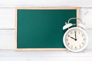 Beyaz ahşap arka planda alarmlı yeşil tahta, boş tahta, zaman yönetimi ve eğitim kavramı.