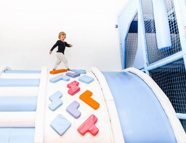 Oğlan çocuk şişme trambolinlerle çocuk odasında oynuyor, kaydırak aktif oyuna tırmanıyor.