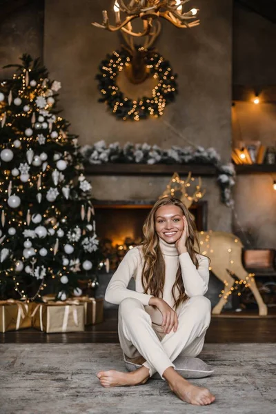 Uzun saçlı, bej takım elbiseli genç ve güzel bir manken. Noel ağacı. Kahverengi ahşap.