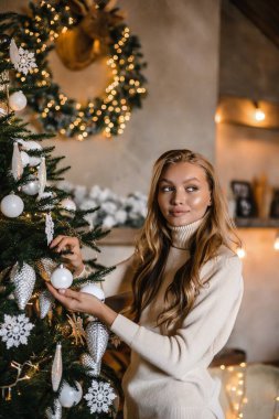 Uzun saçlı, bej takım elbiseli genç ve güzel bir manken. Noel ağacı. Kahverengi ahşap.