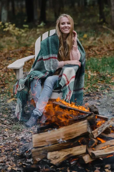 Ateşin yanında oturan genç bir kadın. Renkli, sıcak bir buzun içinde. Uzun saçları ısıtıyor. — Stok fotoğraf
