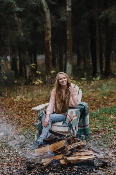 Ateşin yanında oturan genç bir kadın. Renkli, sıcak bir buzun içinde. Uzun saçları ısıtıyor. — Stok fotoğraf