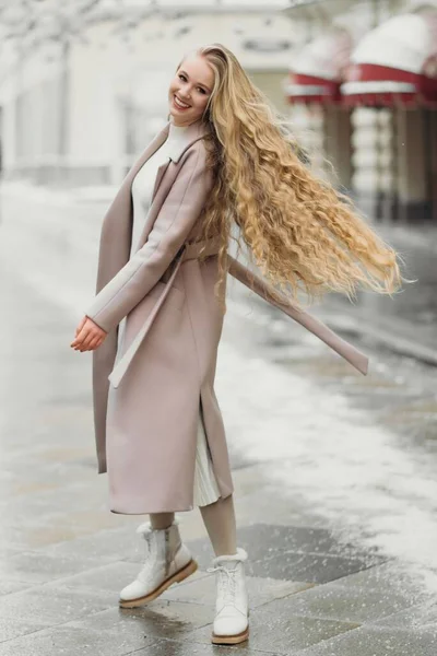 Krásný mladý kavkazský úsměv žena v béžové kabát s dlouhými vlasy chůze venku, — Stock fotografie