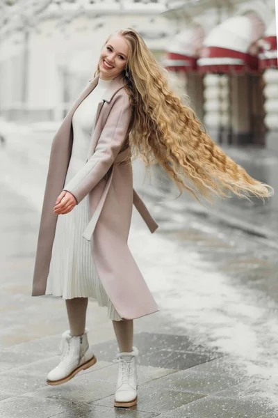 Красива молода біла усміхнена жінка в бежевому пальто з довгим волоссям, що йде на відкритому повітрі , — стокове фото