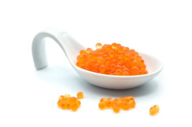 Beyaz arka planda beyaz seramik kaşıkta alabalık yumurtalarının yakın çekimi