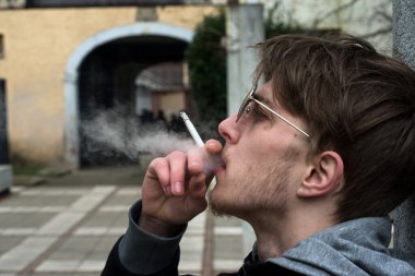 Sokakta sigara içen güneş gözlüklü bir gencin portresi.