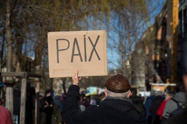 Sokakta savaşı Fransızcada pankartla protesto eden insanlar: Paix, İngilizce gelenek: Barış
