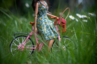 Kamu bahçesinde bisikletli yeşil bir yaz elbisesi giyen esmer manken bebeğinin yakın çekimi. 