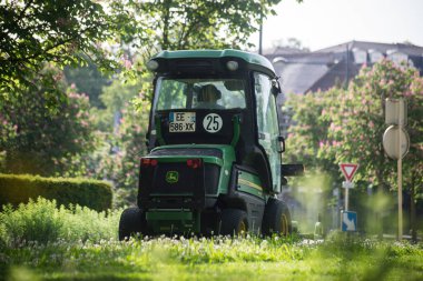 Mulhouse - Fransa - 17 Mayıs 2022 - Şehir parkında yeşil traktör ve çim biçme makinesi kullanan belediye çalışanı