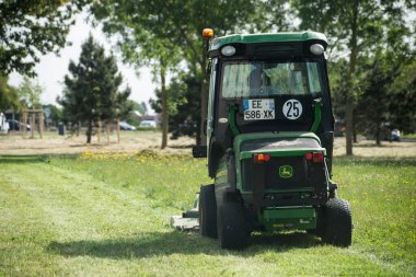 Mulhouse - Fransa - 31 Mayıs 2022 - Şehir parkında yeşil traktör ve çim biçme makinesi kullanan belediye çalışanı 