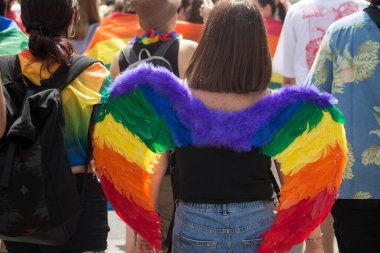 Arka planda, eşcinsel gururu sırasında gökkuşağı kanatları takan genç bir kadının portresi