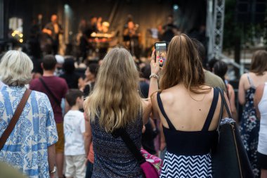 Mulhouse - Fransa - 21 Haziran 2022 - Elinde akıllı telefonuyla bir konserde fotoğraf çeken kızların arka plandaki portresi 