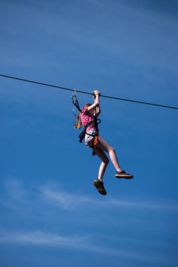 Kruth - France - 8 August 2022 - Portrait of young Woman descend on a zip line on blue sky background