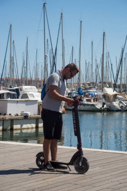 Le cap d'agde - France - 27 July 2022 - Portrait on man standing on electric scooter on harbor background