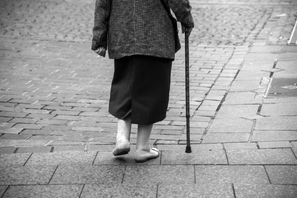 closeup of legs of old woman walking in the street with stick in black and white