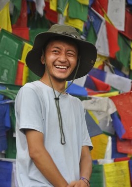 Yanlara bakan mutlu bir Tibetli genç adam, Budist dua bayraklarına karşı duruyor. 