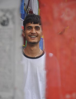 Budist dua bayrakları etrafında dikilirken kameraya bakan mutlu Hintli bir gencin seçici odağı 