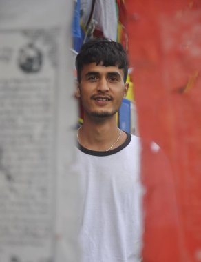 Budist dua bayrakları etrafında dikilirken kameraya bakan Hintli bir gencin seçici odağı 