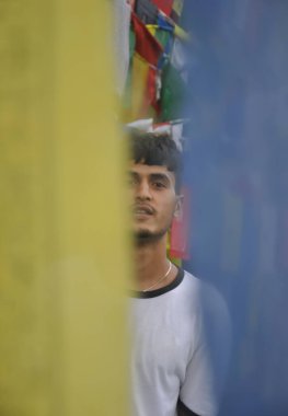 Budist dua bayrakları etrafında dikilirken kameraya bakan Hintli bir gencin seçici odağı 