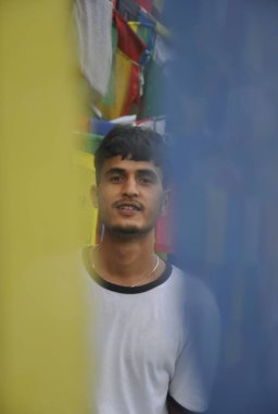 Budist dua bayrakları etrafında dikilirken kameraya bakan Hintli bir gencin seçici odağı 