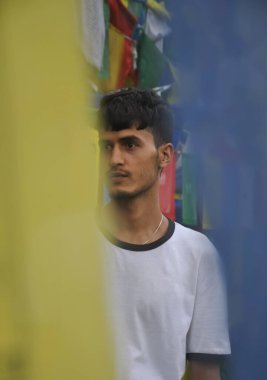 Budist dua bayrakları etrafında dikilirken yan bakan Hintli bir gencin seçici odağı 