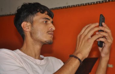 Kapalı mekanda otururken telefonunu kullanan genç bir adamın yakın görüntüsü.