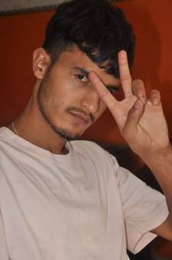 Yakışıklı bir delikanlının, elinde barış işareti olan, kapalı bir yerde oturmuş kameraya bakarken yakın plan çekimleri.