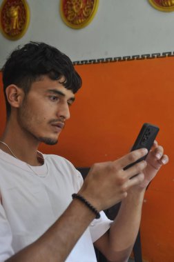 İçeride otururken telefonu kullanan yakışıklı bir gencin yan görüntüsü.