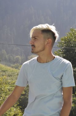 Beyaz saçlı Güney Asyalı bir genç fotokopi çektirirken yan tarafa bakıyor.