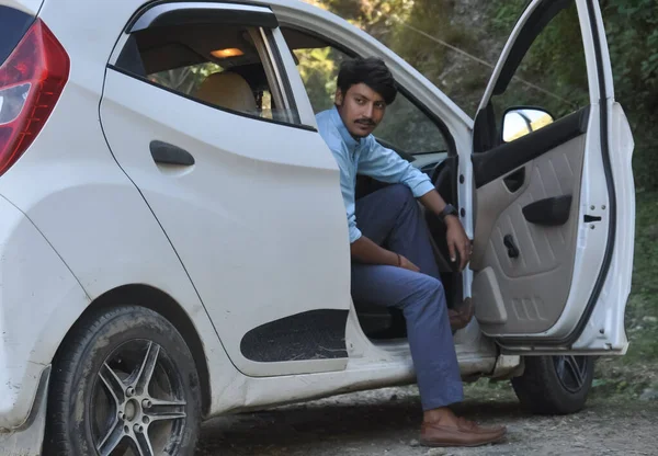 車の中でドアを開けて座っている間に横に見えるハンサムな若いインド人の男 — ストック写真
