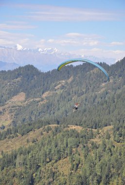 Mandi, Himachal Pradesh, Hindistan - 10 16 2021: Dağ ve buzul manzaralı profesyonel pilotla yamaç paraşütü yapan genç bir adam