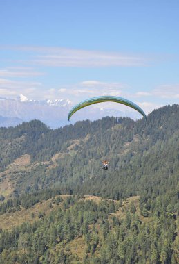 Mandi, Himachal Pradesh, Hindistan - 10 16 2021: Dağ ve buzul manzaralı profesyonel pilotla yamaç paraşütü yapan genç bir adam