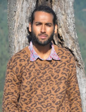 Ağaca yaslanırken kameraya bakan sakallı bir gencin ön görüntüsü.  