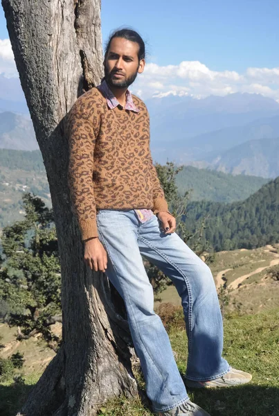 丘陵地帯の木にもたれながら横に見える良い南アジアの若い男性の完全な長さ — ストック写真