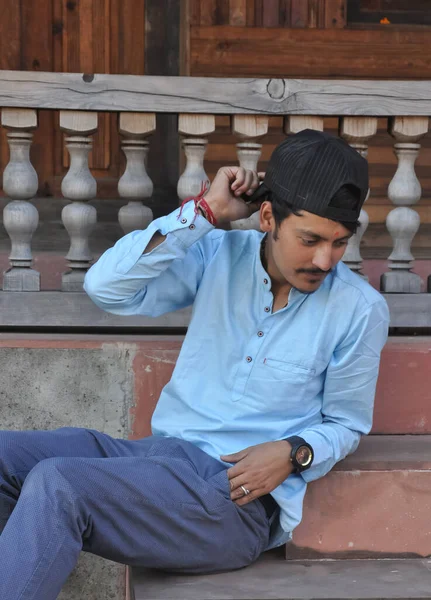 寺の階段に座っている間下を見下ろすと彼の帽子に触れる良い見て北インドの若い男の側面図 — ストック写真