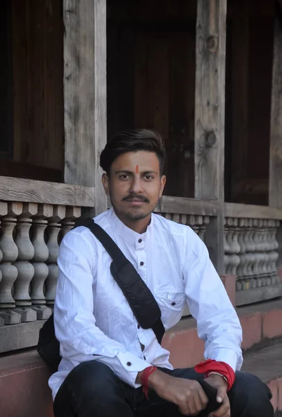 A good looking Indian young guy looking at camera while sitting on temple stairs