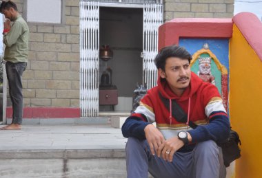 Arka planda Tanrı 'ya tapan bir adamla merdivenlerde otururken yan bakan bir gencin yakın çekimi. 