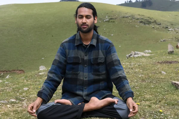 Front view of a young Indian guy practicing Meditation, Yoga in Lotus Pose (Padmasana) with Gyan Mudra (Gesture of Knowledge) in the mountain.