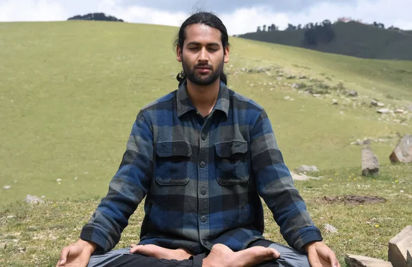 Front view of a young Indian guy practicing Meditation, Yoga in Lotus Pose (Padmasana) with Gyan Mudra (Gesture of Knowledge) in the mountain.