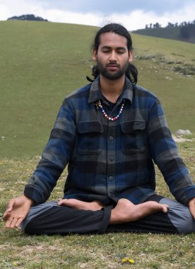 Front view of a good looking Indian young man practicing Yoga in Lotus Pose (Padmasana) with Gyan Mudra (Gesture of Knowledge) in the mountain.