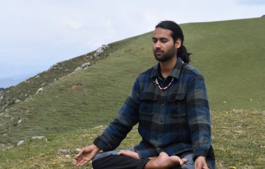 A young Indian man practicing Yoga in Lotus Pose (Padmasana) with Gyan Mudra (Gesture of Knowledge) in the mountain.