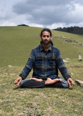 Front view of a Indian young man practicing Yoga in Lotus Pose (Padmasana) with Gyan Mudra (Gesture of Knowledge) in the mountain.