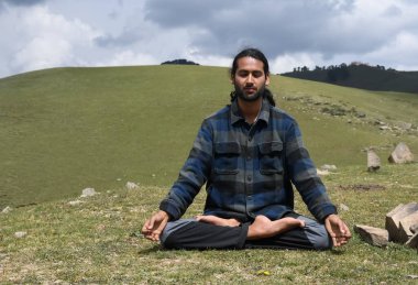 Front view of a Indian young man practicing Yoga in Lotus Pose (Padmasana) with Gyan Mudra (Gesture of Knowledge) in the mountain.