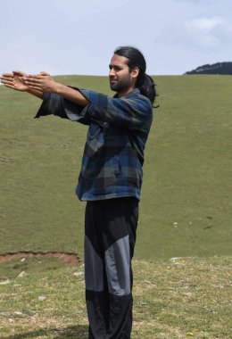 A young Indian guy warm up his body with doing Front Arm Raise exercise in the mountain.  