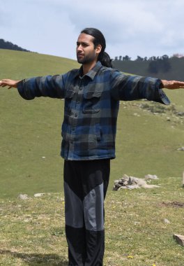 A good looking young Indian guy doing Side Arm Raise exercise in the mountain.  